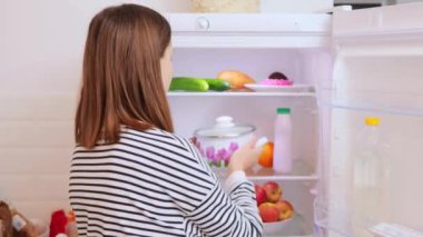 Kahverengi saçlı kadın çizgili gömlek giyiyor. Buzdolabını açıyor. Bozuk çorbayla esrar içiyor.