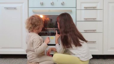 Mutlu kız kardeşler gaz fırınının yanında rahat çocuklar giyerek oturmuş lezzetli turtaları bekliyor birlikte eğleniyor ve ev yapımı pastaların tadını çıkarıyorlar.