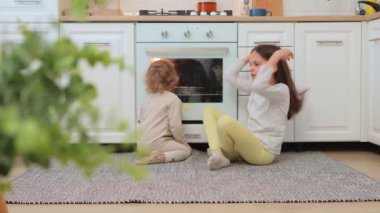 Mutlu çocuklar gaz fırınının yanında oturmuş lezzetli bir turtayı bekliyorlar. Birlikte eğleniyorlar. Mutfakta fırında harika bir aile anı izliyorlar.