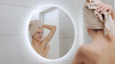 Kadınsal sağIık. Vücut tedavisi. İyi olmak rutin bir şey. Kafası havluya sarılı beyaz bir kadın aynaya bakıyor. Yansımasına bakıyor. Koltuk altını jiletle kurtarıyor.
