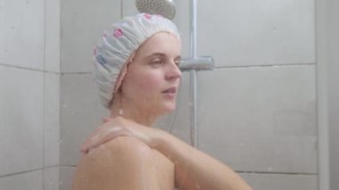 Genç, güzel, çıplak bir kadın banyoda duş alıyor. Duş başlığı takıyor, sabah hijyen rutini yapıyor. Vücut temizliğiyle ilgileniyor.