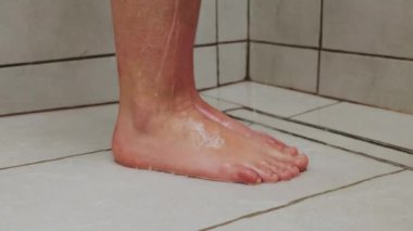 Banyodaki kimliği belirsiz beyaz fayansla yıkanmış, duş kabininde tanınmayan bir kadın ayak hijyenik prosedürler uyguluyor.