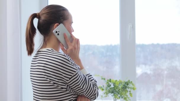 Kahverengi Saçlı Atkuyruklu Sıradan Çizgili Tişörtlü Telefonda Konuşan Pencerenin Yanında — Stok video