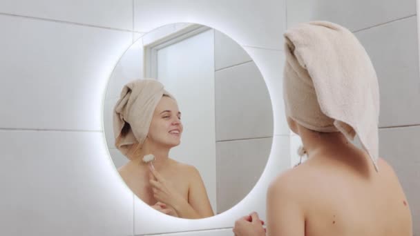 化妆品的程序 清除常规 面部水疗 白种人女人头上裹着毛巾 用按摩棒擦拭面部皮肤 看着镜子里的倒影 — 图库视频影像