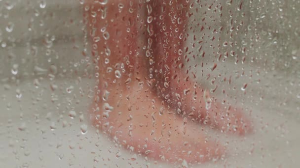健康と衛生について 水滴でぼやけたガラスの後ろに立っている少女の足 認識できない女性がシャワーを浴びる — ストック動画