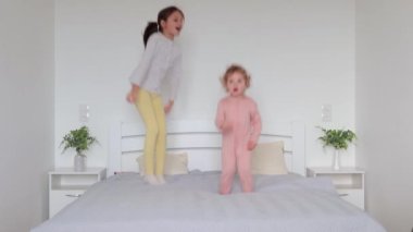İki kız kardeş pijama giyip yatağa atlıyor ve ebeveyn odasında eğleniyorlar. Evde, yumuşak, sıcak pijamalarıyla mutlu anların tadını çıkarıyorlar.