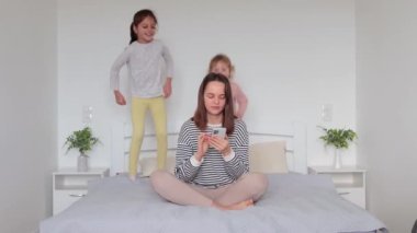 Kahverengi saçlı, rahat gömlekli bir kadın. Annesi evde akıllı telefon kullanıyor. Kız dans ediyor, zıplıyor, eğleniyor.