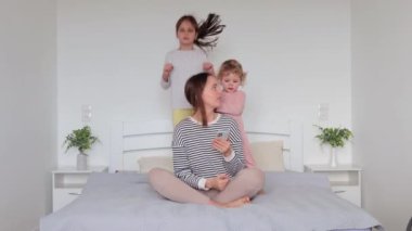 Sinirli, beyaz bir kadın çizgili tişört giyiyor. Gürültülü çocukları zıplarken ve annesinin dikkatini çekmeye çalışırken cep telefonu kullanıyor.