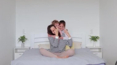 Mutlu anne ve kızlar evde yatakta birlikte eğleniyor ve eğleniyorlar. Hafta sonları boş vakitlerin tadını çıkarıyorlar. Birbirlerine gülümseyen yüzlerle sarılıyorlar.