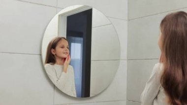 Banyoda poz veren sevimli ve çekici bir kız. Aynanın önünde sabah güzellik ameliyatı yapıyor. Yüz derisini temizlemek için sünger kullanıyor.