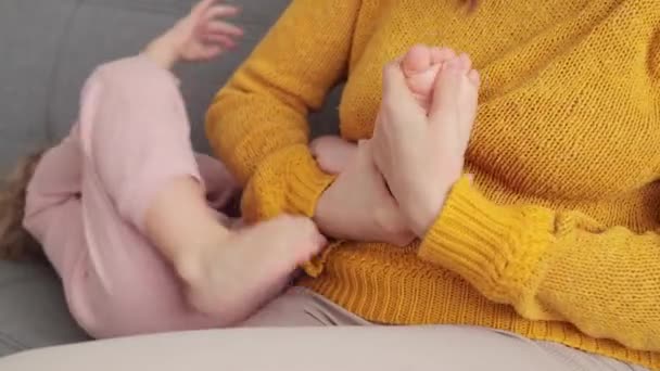 穿着黄色毛衣的不明身份的女人年轻的妈妈一边在客厅里坐着咳嗽一边按摩小宝宝的脚 — 图库视频影像