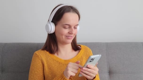 Vreedzame Bruinharige Vrouw Moderne Draadloze Hoofdtelefoon Ontspannen Comfortabele Bank Luisteren — Stockvideo