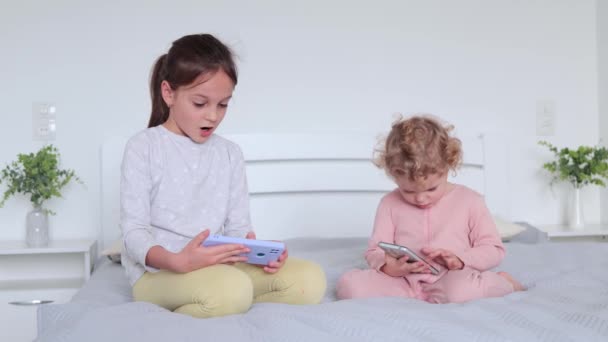 Two Little Sisters Playing Mobile Phones While Sitting Bed Bedroom — Stock Video