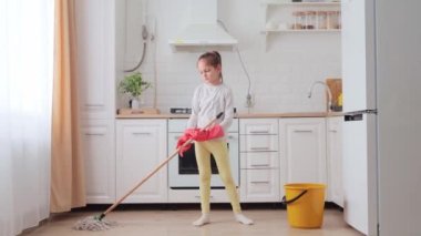 Ev ıslak temizleme. Sıkıcı, lastik eldivenli küçük bir kız mutfakta paspas yıkıyor, mutfağı temizliyor ve mutsuz bir yüz ifadesi var.