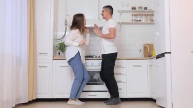 Mutfakta dans ederken el ele tutuşan ve birbirlerine bakıp yeni evlerinde sevgi ve mutluluk ifade eden neşeli beyaz bir çift.