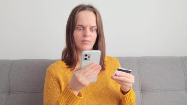 Şen şakrak beyaz kadın, sarı kazak giyen, akıllı telefon ve kredi kartıyla koltukta oturan ve internetten yemek siparişi veren başarılı bir alışveriş yapan.