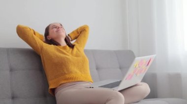 Çekici, beyaz bir kadın dizüstü bilgisayar kullanıyor. Evdeki kanepede oturup çalışıyor. Bir dakika dinleniyor, bilgisayar başında dinleniyor.