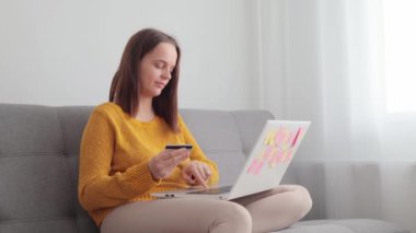 Mutlu Kafkasyalı çekici kadın gündelik giysiler giyip kanepede dizüstü bilgisayar ve kredi kartıyla oturuyor. İnternetten alışveriş siparişleri alıyor. Yemek siparişi veriyor, yumruklarını sıkmış başarılı bir şekilde eğleniyor.