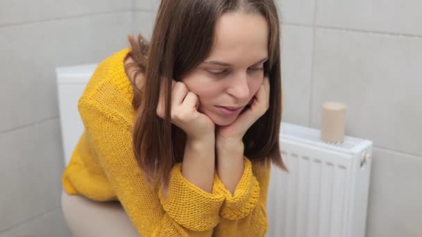 浴室のトイレボウルに座っている黄色いジャンパーのブラウンハイレッドコーカサス女性は胃に悪い消化器系便秘の下痢の食物中毒を持っています — ストック動画
