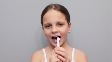 Diş sağlığı eğlencesi. Elektrikli fırça heyecanı. Gri arka planda izole edilmiş elektrikli diş fırçasıyla dişlerini fırçalayan komik kahverengi saçlı küçük kız.