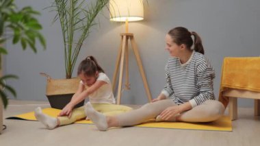 Yoga ve oyun zamanı. Aktif ebeveynlik yolculuğu. Sevgiyle jimnastik. Beyaz kadın ve küçük kızı birlikte spor yapıyorlar. Vücutlarını esneterek evde esneklik kazanıyorlar.