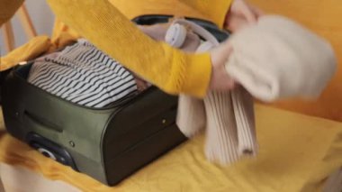 Sarı kazaklı, sırt çantalı, tanınmayan bir gezgin. Tatilden ya da yolculuktan sonra valizdeki giysileri ve eşyaları boşaltıyor.