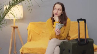 Genç, düşünceli bir kadın tatil bütçesi planlıyor. Gerekli alışverişler için para dağıtıyor. Kanepede oturup gelecek turları ve para harcamalarını düşünüyor.