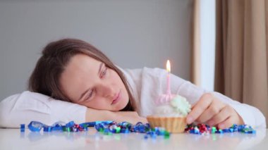 Doğum günü partisi üzüntüsü. Kafkasyalı genç bir kadın masaya oturmuş yılanbalığıyla süslenmiş aydınlık odada yanan mumla doğum günü pastasına bakıyor.