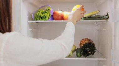 Buzdolabı tazelik dolu. Kahverengi saçlı kadın buzdolabını açıyor sağlıklı yemek için meyve ve sebze yiyor taze sebze ürünleriyle düzgün beslenme yemekleri hazırlıyor.