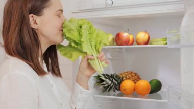 Sağlıklı beslenmeyi seven mutlu bir kadın diyet sebzeleri pişirmek için taze sebzeleri buzdolabından alıyor lezzetli kahvaltılar hazırlamak için buzdolabından ürünler alıyor.