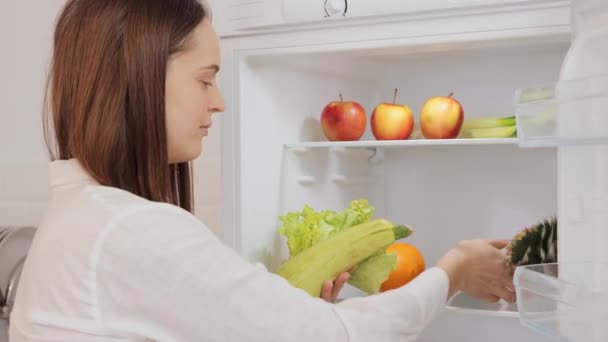 新鮮で冷たい果物と野菜で満たされた家庭用冷蔵庫を組織する女性は栄養価が高くバランスの取れた食事を維持するための冷凍の利点を示しています — ストック動画
