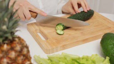 Tanınmayan bir kadın aşçı, salatalık salatası salatalık, sebze, ahşap kesme tahtası mutfak masasında sağlıklı organik gıda hazırlıyor.