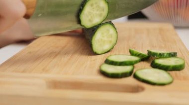 Tanımlanamayan bir kadın mutfakta bıçakla yeşil salatalıkları kesiyor sağlıklı sebzeli salata hazırlıyor organik yemek pişirmek için dilimlere ayırıyor.