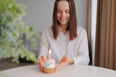 Çekici, iyimser, genç, beyaz saçlı, doğum gününü pasta ve mumla kutlayan kadın tatilinin tadını çıkarmayı düşünüyor.