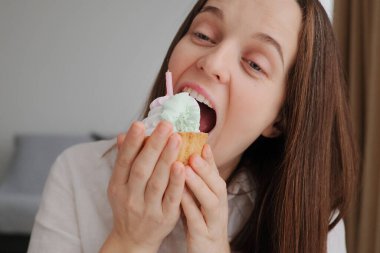 Kahverengi saçlı, iştah açıcı kremalı pasta yiyen güzel bir kadın, doğum günü kutlamasında lezzetli bir tatlı yeme arzusuna kapılır.