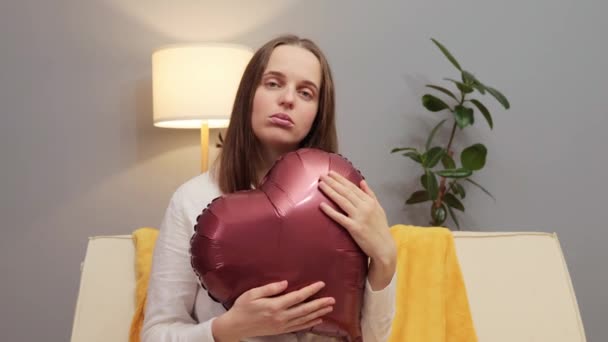 悲伤的成年女子独自抱着心形气球在房间里 有感情问题 带着沮丧的表情庆祝情人节 感到孤独 — 图库视频影像