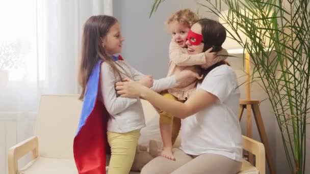Radosna Kobieta Masce Superbohatera Bawiąca Się Córkami Domu Siedząca Kanapie — Wideo stockowe