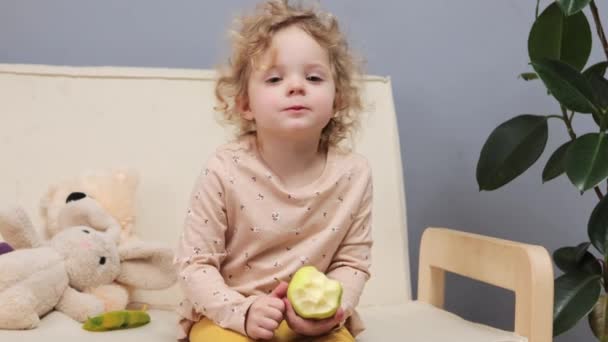 Encantadora Niña Linda Rubia Pelo Ondulado Sentada Sofá Comiendo Manzana — Vídeos de Stock