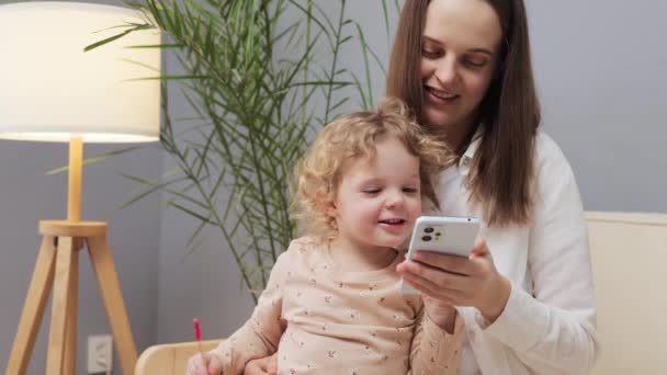 Fröhliche Braunhaarige Frau Sitzt Mit Ihrem Kleinkind Auf Dem Sofa — Stockvideo