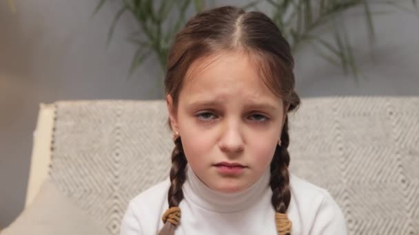 小女孩不高兴地穿着白色的高领毛衣 辫子坐在沙发上 看着摄像机准备哭泣 却被激怒了 她很不高兴 — 图库视频影像