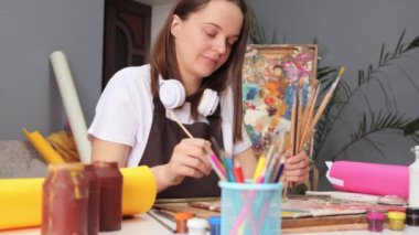 Profesyonel sanatçılık gösterisi. Güzel sanatlar ve el sanatları. Çağdaş resim teknikleri. Kafkasyalı kadın sanatçı, işyerindeki tuvalde boya fırçasıyla suluboya resim yapıyor.