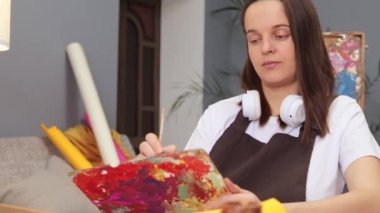 Suluboya resim teknikleri. Çağdaş sanatta ustalık. Eğitim sanatı dersleri ve atölyeler. Çağdaş stüdyoda fırçayla boyalı beyaz saçlı kadın ressam.