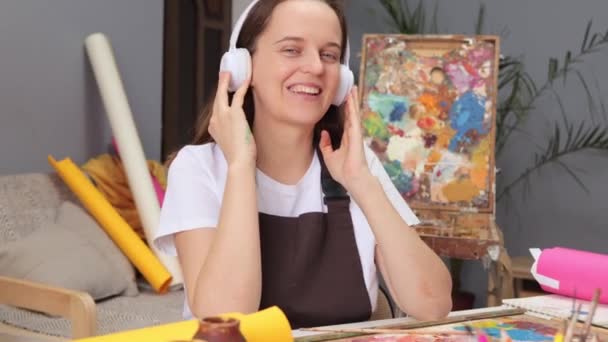 绘画和绘画作为一种工具 教育艺术课和讲习班 当代画室里的白种人棕色头发的女画家 用耳机听音乐 — 图库视频影像