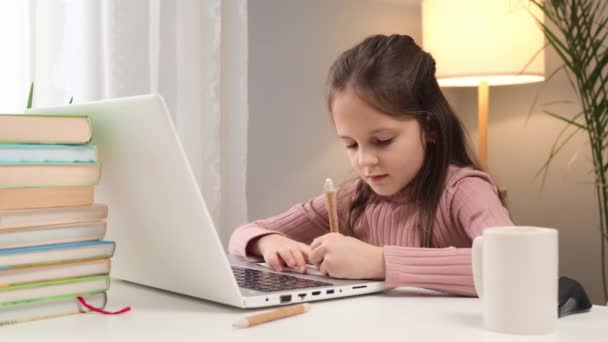 用笔记本电脑远程学习 在线学习的表格设置 参加虚拟课程的孩子 白种人棕色头发的小女孩在家里用笔记本电脑写下在网上学习的任务 — 图库视频影像