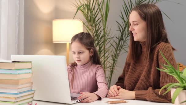 妈妈用电脑教孩子 孩子们的在线学习 一起在家学习 使用笔记本电脑的电子学习课程 白种人的母亲和小女孩坐在桌旁 — 图库视频影像