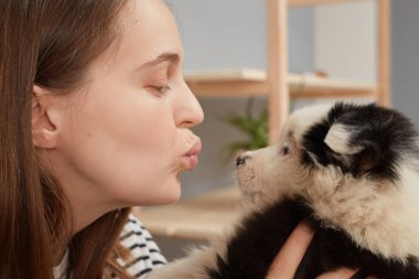 Yan görüntüde, çizgili tişört giyen beyaz, şirin bir kadın siyah beyaz köpeğini öperken evinde yeni evcil hayvanıyla oynuyordu.