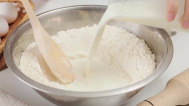 Tanınmayan kadın fırıncı hamura süt ekliyor, yavaşça karıştırıyor, hamuru ekmek pişirmek için hazırlıyor.