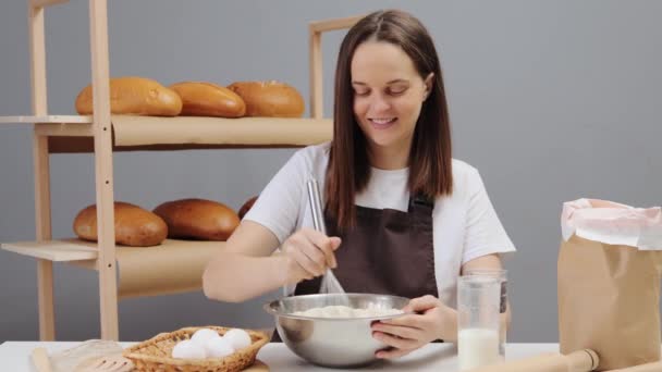 彼女の仕事を楽しむパン焼きのための食材を混ぜる彼女の職場に座って茶色のエプロンを身に着けている陽気な女性のパン屋 — ストック動画