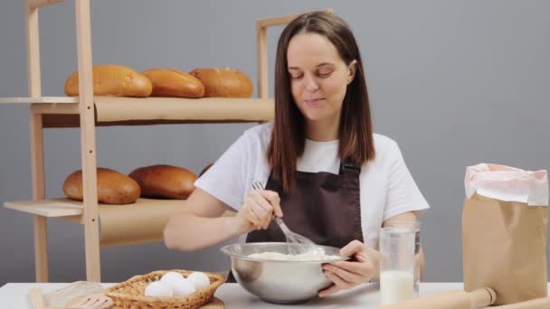 パンを作ったり歌ったり誰かと話したりするために茶色のエプロンを混ぜたハッピーな陽気な女性パン屋 — ストック動画