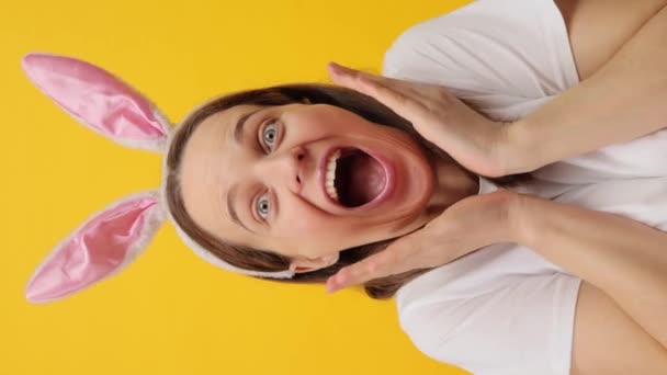 バーティカルビデオ 黄色の背景に隔離されたウサギの耳のヘッドバンドを身に着けている驚くべき白人女性は Omgを興奮するイースターの休日の素晴らしいお祝いを喜びます — ストック動画